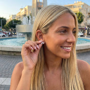 דוגמנית בלונדינית מחייכת ועונדת עגיל כסף צמוד בצורת כתר עם זירקונים על רקע מזרקה עירונית